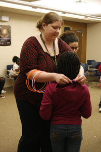A volunteer fastens a glowstick necklace around a girl's neck