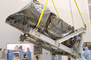 Inside Hangar AE at Cape Canaveral Air Force Station (CCAFS), an overhead crane raises the Swift spacecraft, wrapped in a protective cover, to vertical before being placed on a work stand.